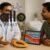 A doctor talking to a male patient in a clinic while a tablet on the table displays a diagram of healthy blood vessels and nitric oxide, with a sliced papaya placed beside them.